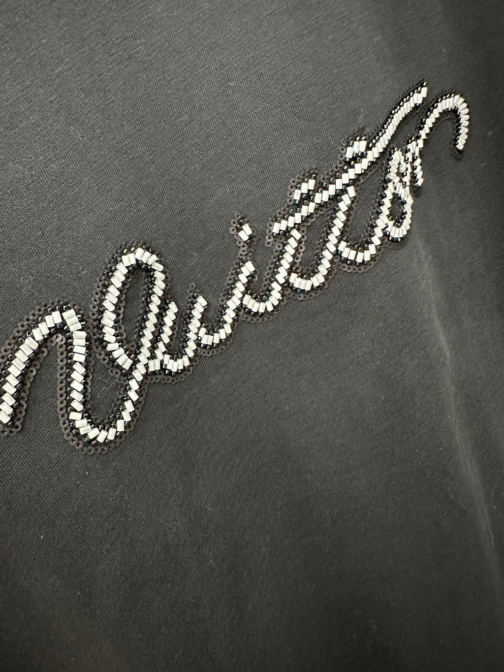 Close-up of white Louis Vuitton script logo on a dark T-shirt