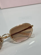 Gold sunglasses showing temple hinge and amber-tinted lenses, round cat-eye frame