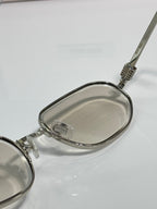 Silver metal sunglasses close-up with clear lenses and patterned temple hinge