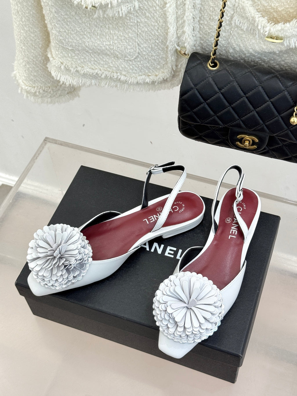 Chanel slingback flats with white flower pom-poms and maroon insoles on a box