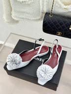 Chanel slingback flats with white flower pom-poms and maroon insoles on a box