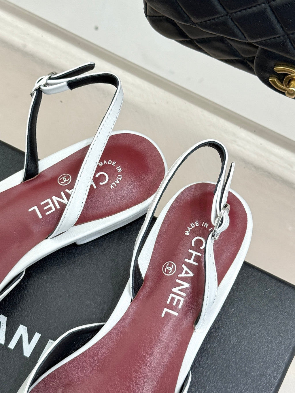 Chanel slingback flats with white straps and maroon insoles on a black box