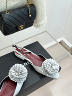 Chanel slingback flats with white flower appliqués on black box, angled view