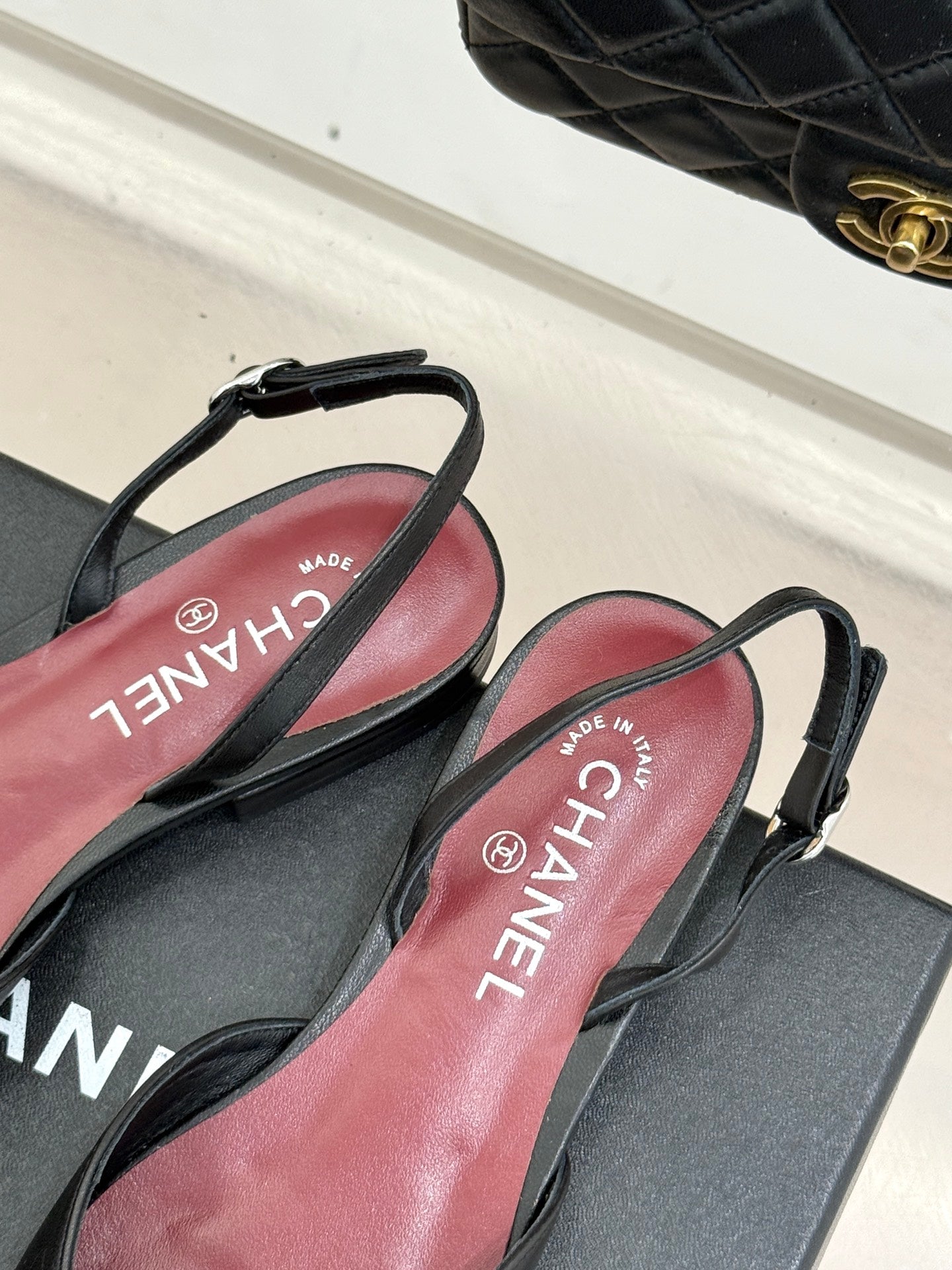 Black Chanel slingback flats with pink insoles and straps, shown on shoe box