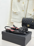 Black Chanel slingback flats with gray flower appliqués on a dark shoe box