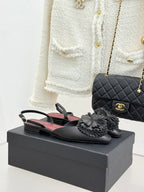 Black Chanel slingback flats with gray flower appliqués on a dark shoe box