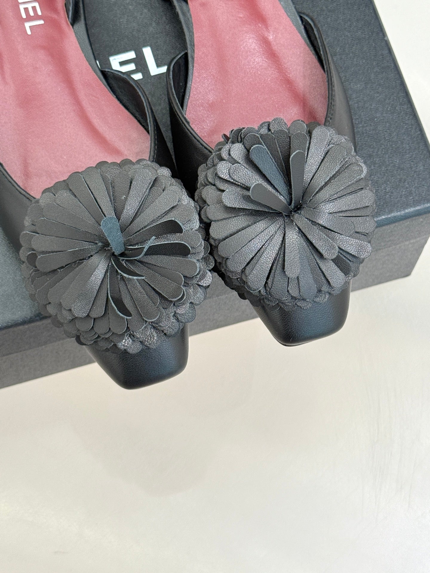 Close-up of black slingback flats with large gray flower appliqués over toes