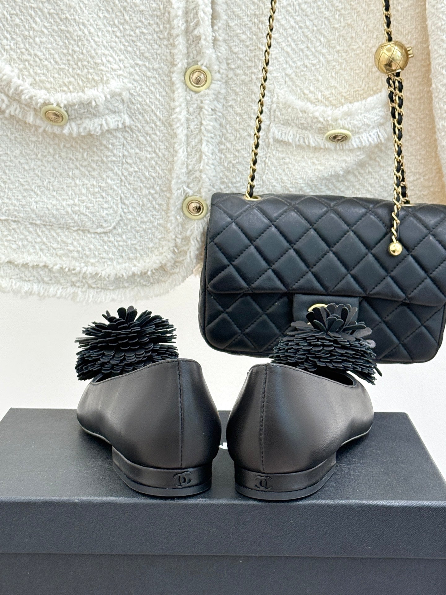Chanel dark flats with gray pom-pom flower details, heel view