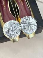 Close-up of gold Chanel flats with white fabric flower toe details