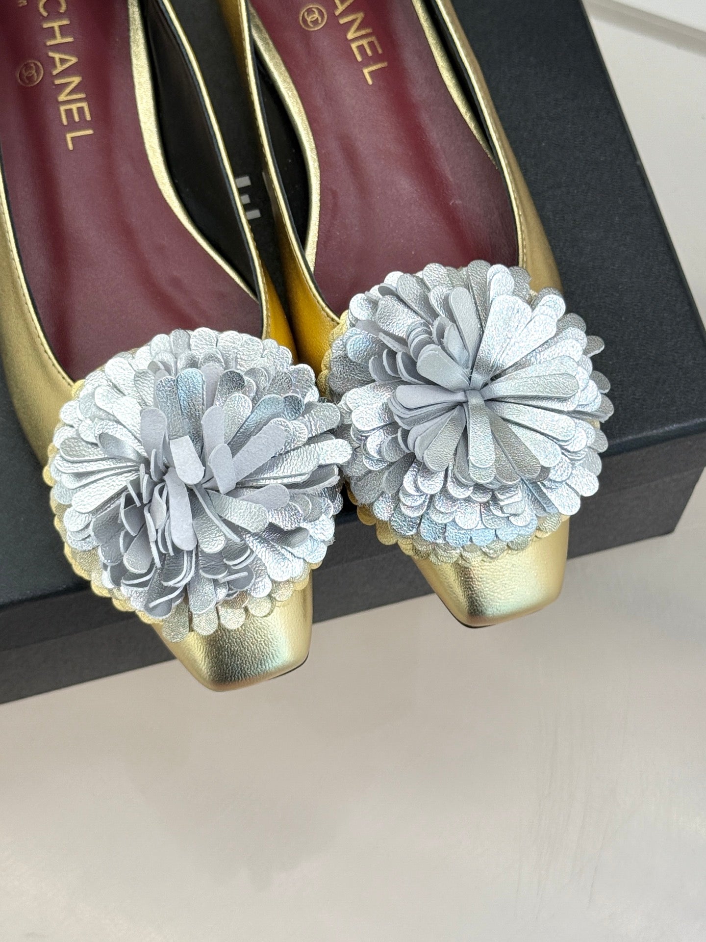 Close-up of gold Chanel flats with white fabric flower toe details