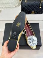 Gold Chanel flat sole and shoe with white fabric flower, held in hand