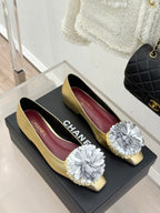 Two gold Chanel flats on a box, showing CHANEL printed burgundy insoles