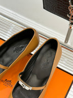 Tan pointed-toe heeled pumps with black lining, ankle strap and buckle detail.