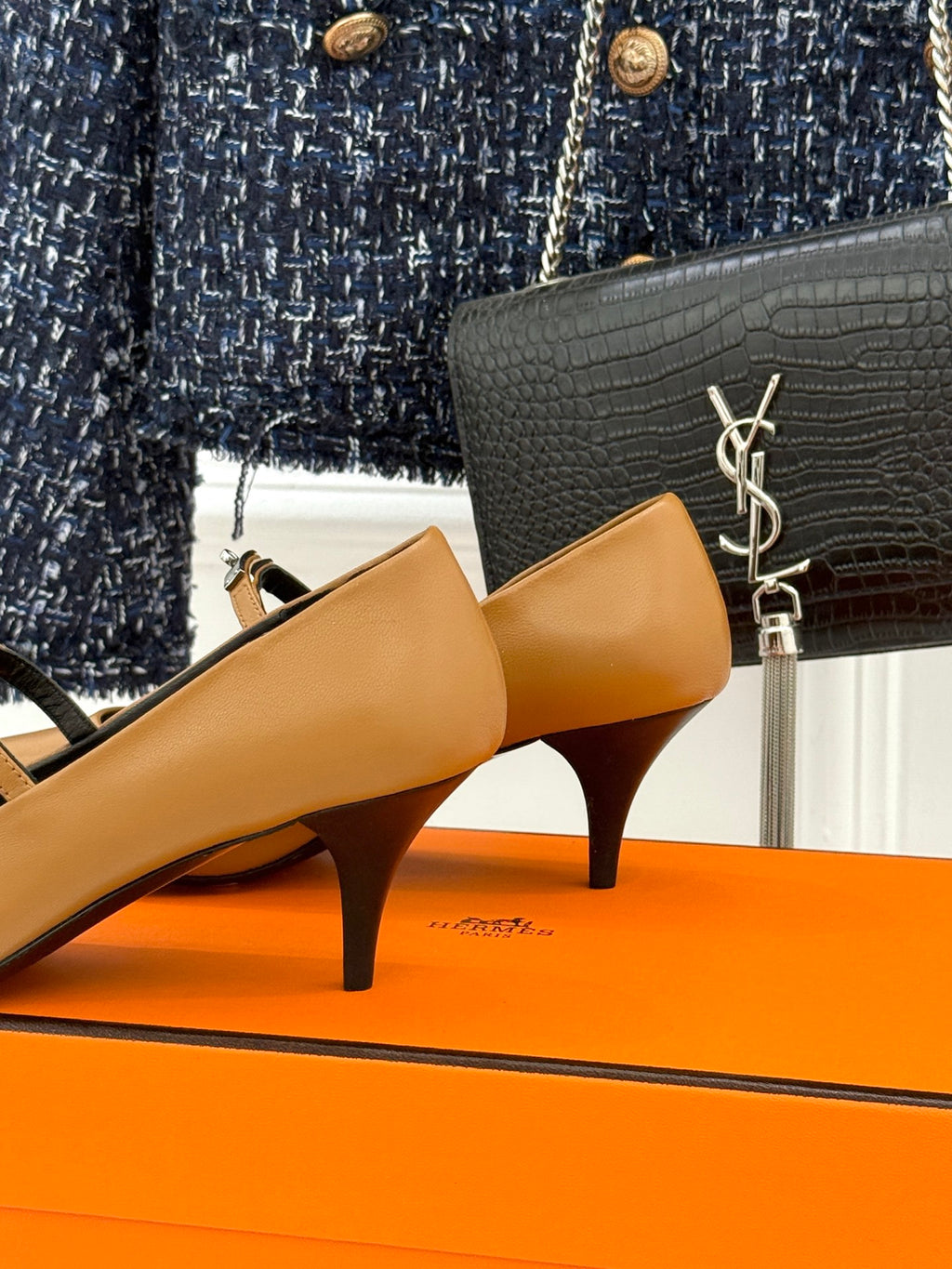 Tan heeled pump with pointed toe and ankle strap, close-up on orange box.