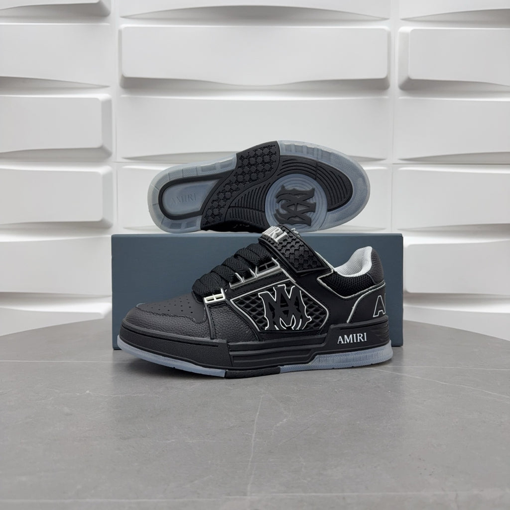 Black low-top sneakers with light gray outsole visible, side emblem and lace strap