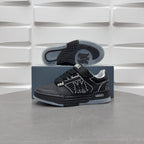 Black low-top sneakers with light gray outsole visible, side emblem and lace strap