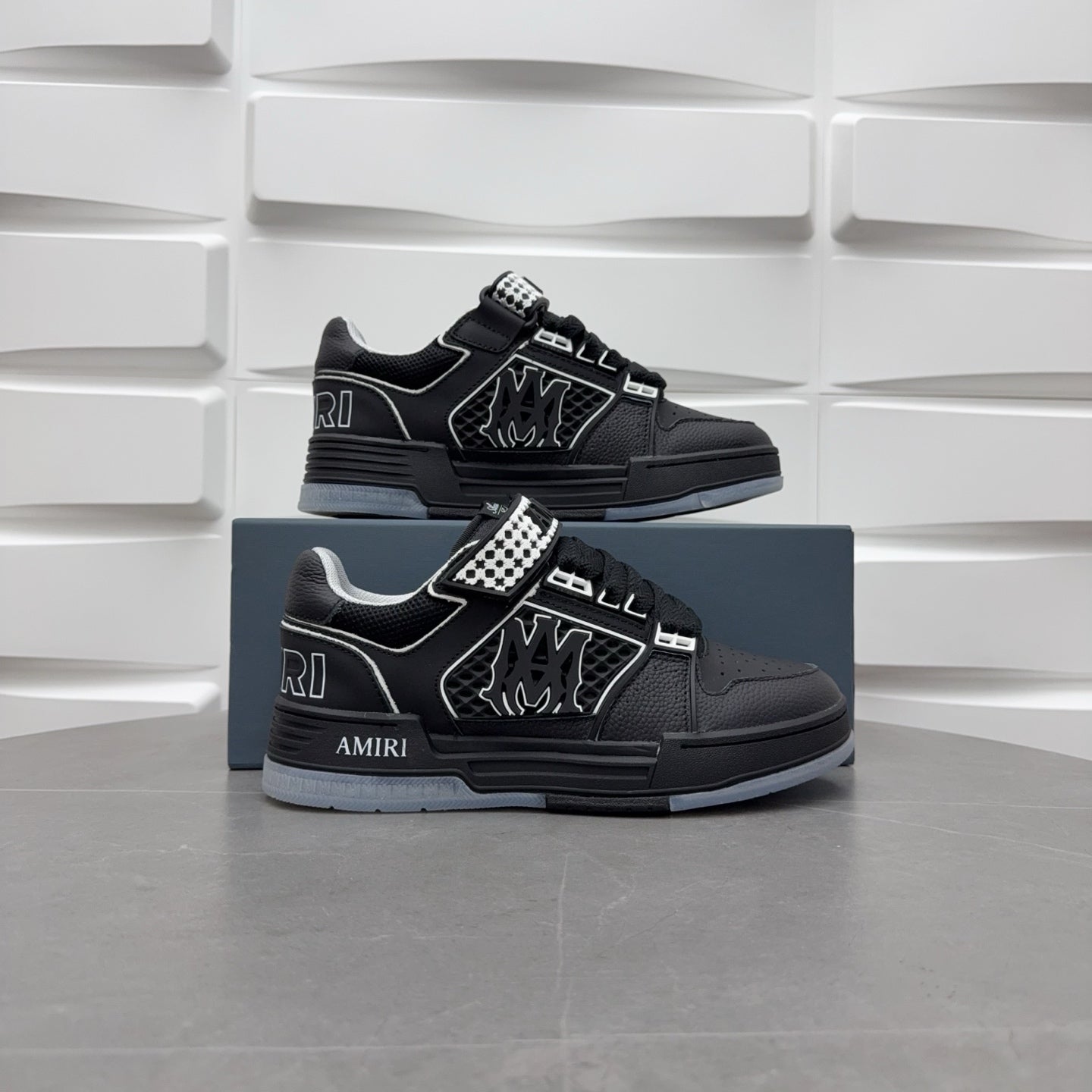 Pair of black low-top sneakers with checkerboard strap and graphic logo, on box.