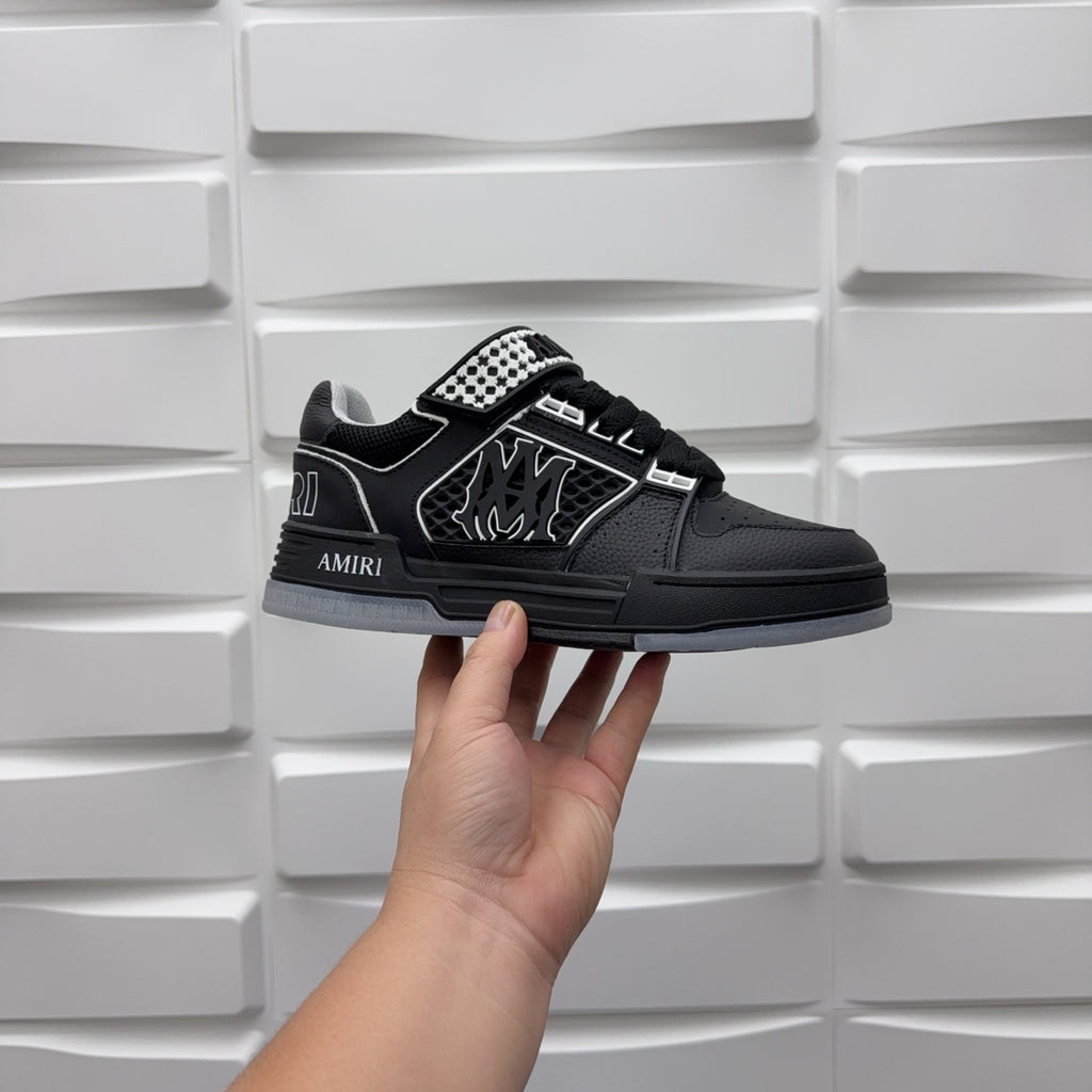 Black low-top sneaker with checkerboard strap detail and graphic logo, held by hand.