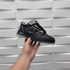 Black low-top sneaker with checkerboard strap and embossed graphic logo, side view.
