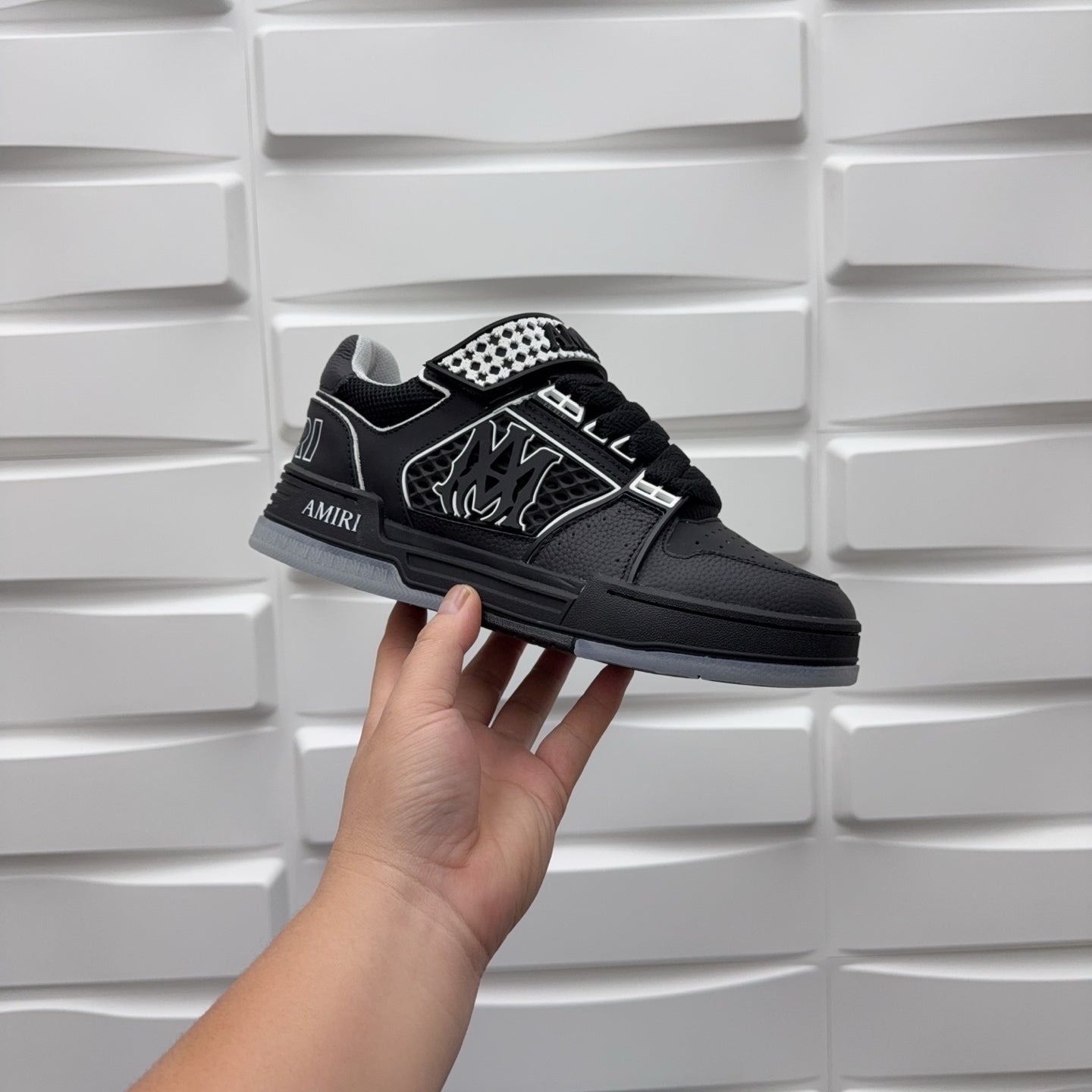 Black low-top sneaker with checkerboard strap and embossed graphic logo, side view.