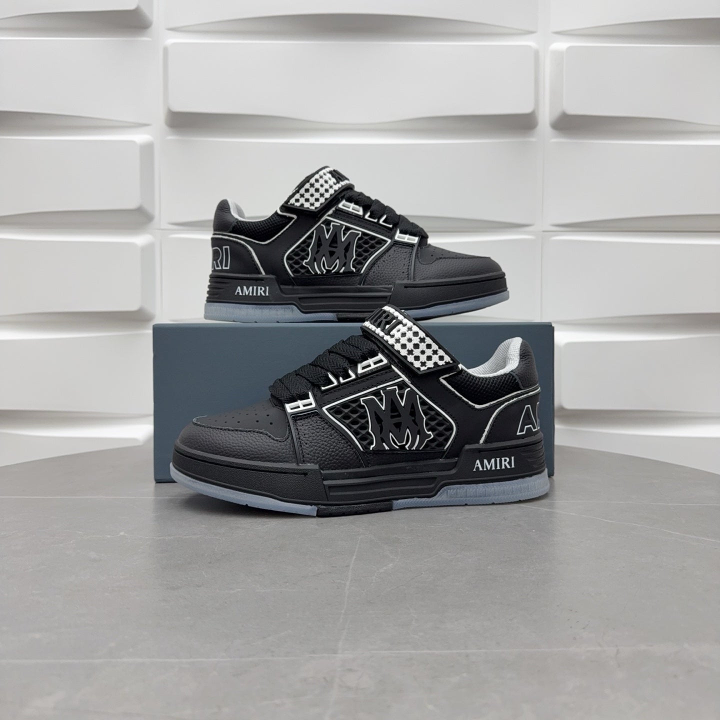 Two black low-top sneakers on box with checkerboard strap and graphic logo.