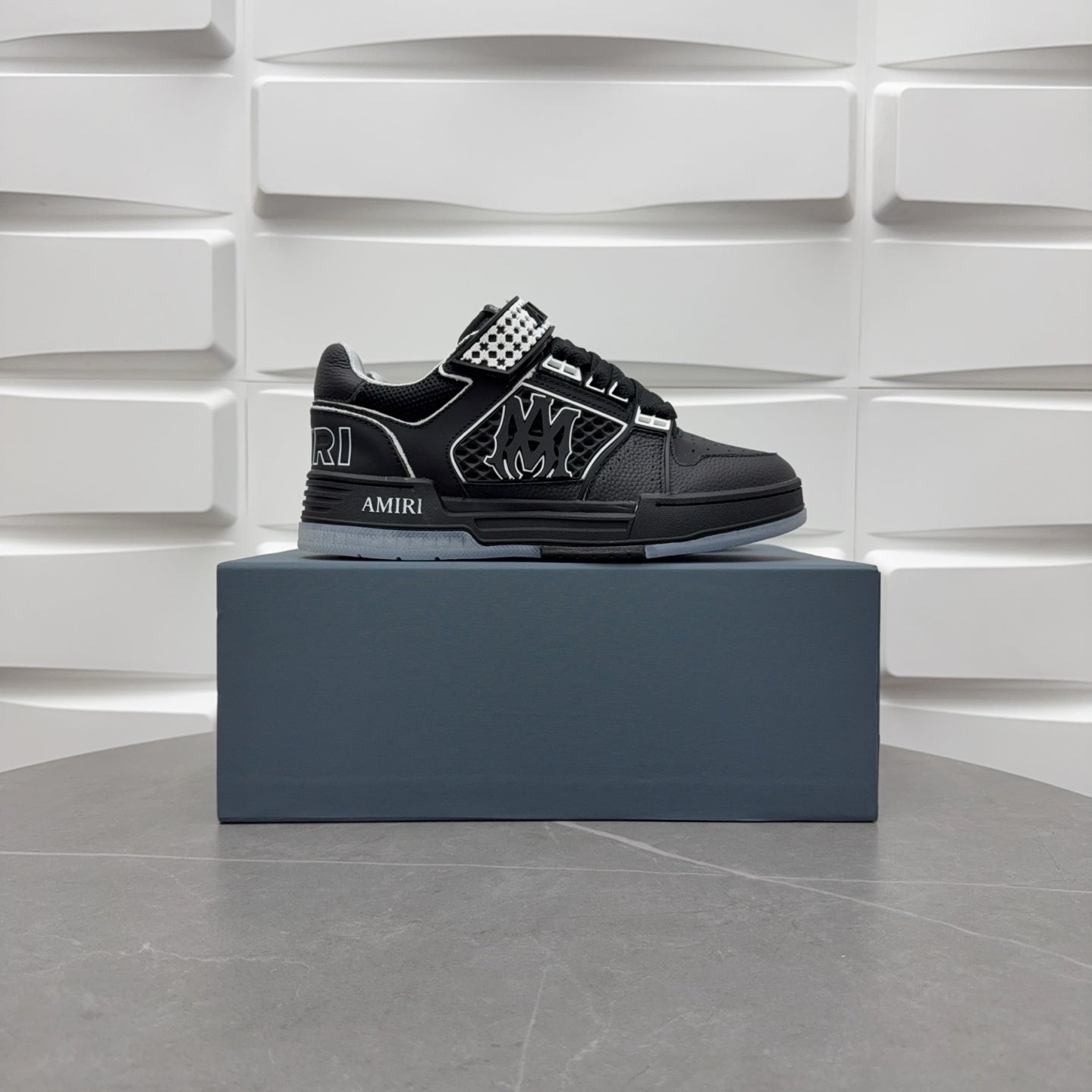 Black low-top sneakers with checkerboard strap and bold graphic logo, on box.
