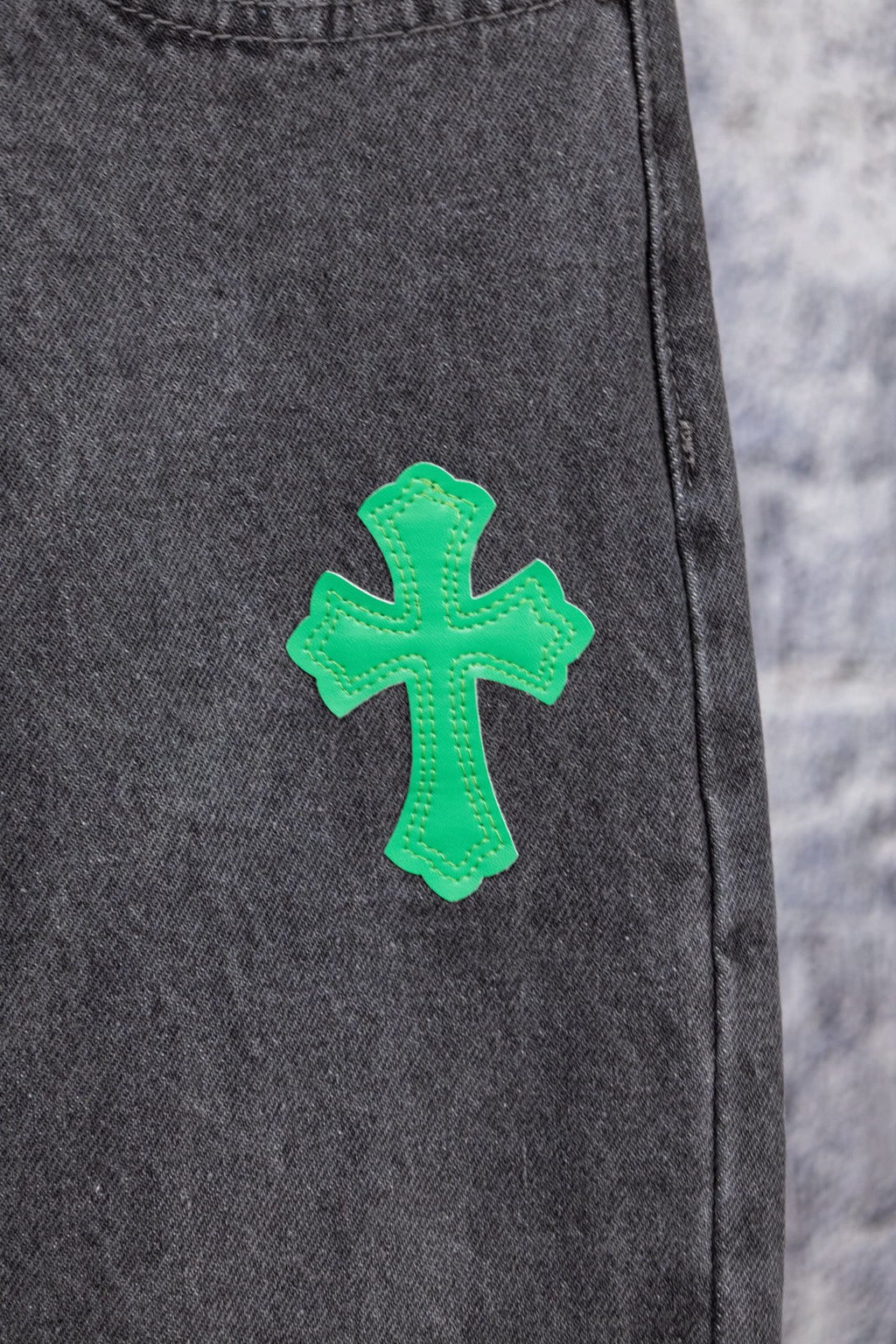 Dark gray denim pants leg with a green cross patch