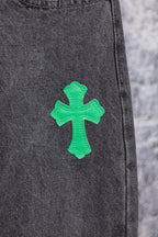 Dark gray denim pants leg with a green cross patch