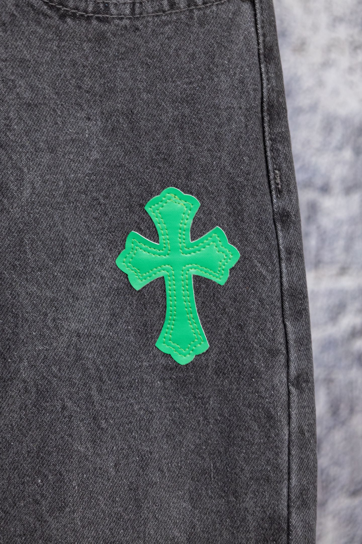 Dark gray denim pants leg with a green cross patch