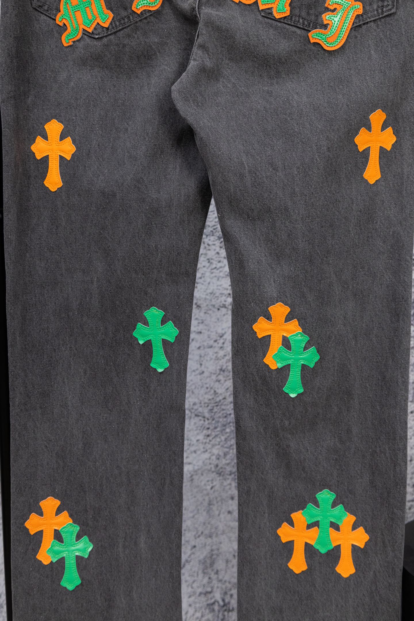 Dark gray denim pants with scattered green and orange cross patches