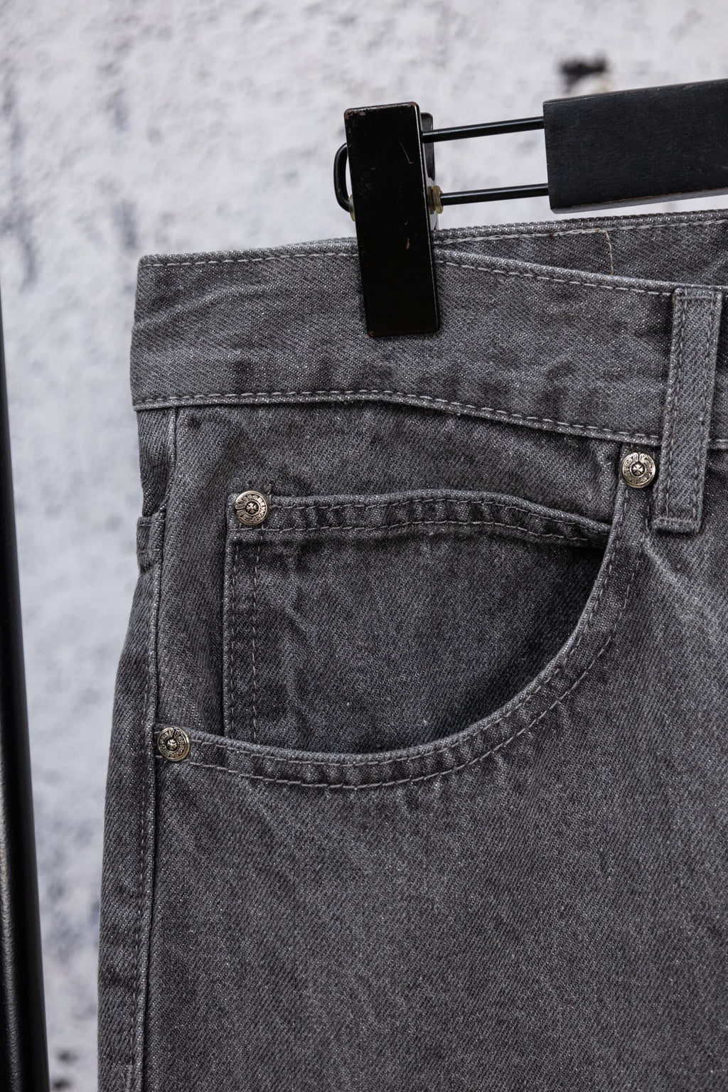 Dark gray denim pants with curved front pocket and metal button details