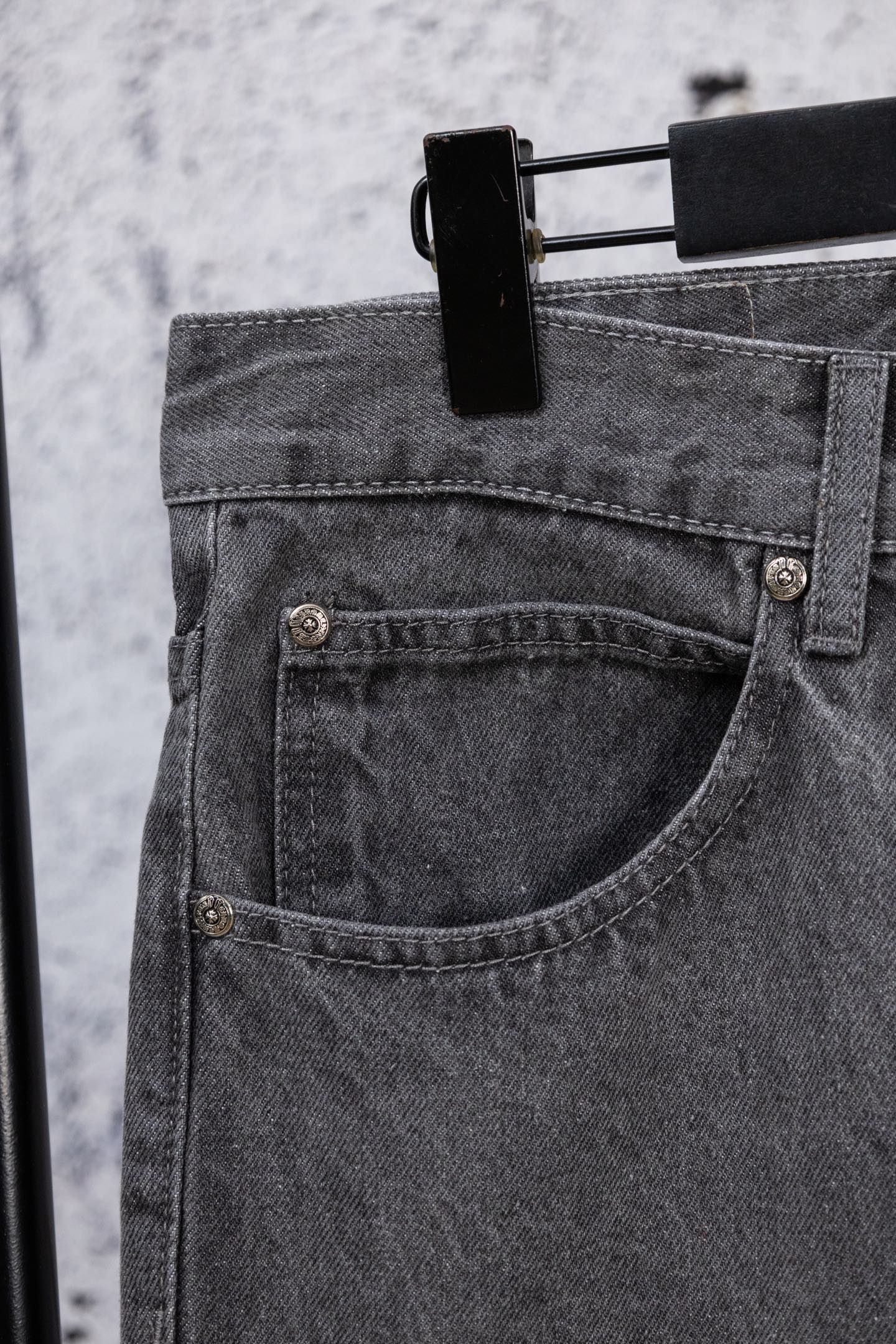 Dark gray denim pants with curved front pocket and metal button details