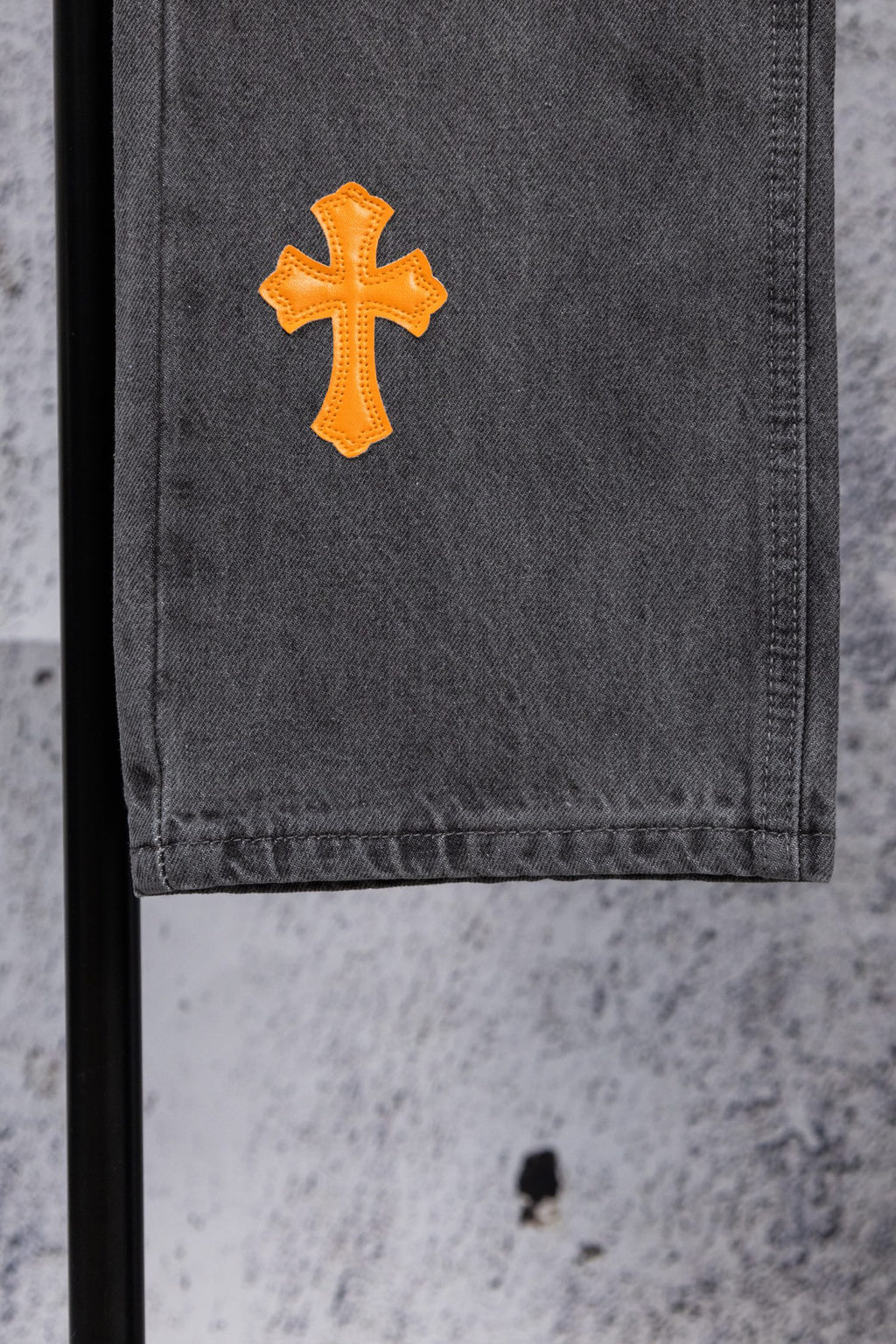 Dark gray denim pants leg with a single orange cross patch