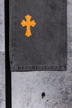Dark gray denim pants leg with a single orange cross patch
