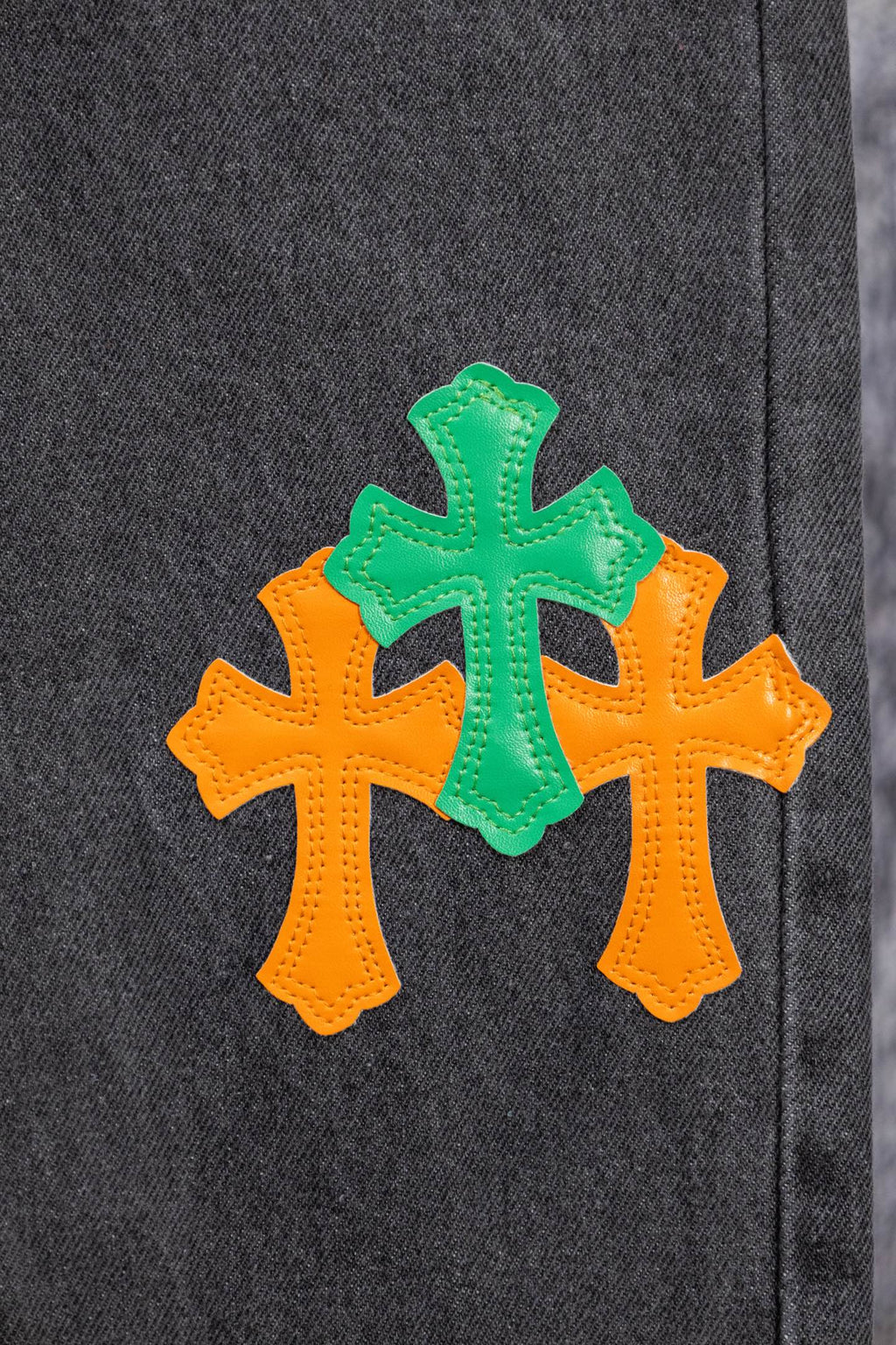 Dark gray denim pants with three cross patches in orange and green