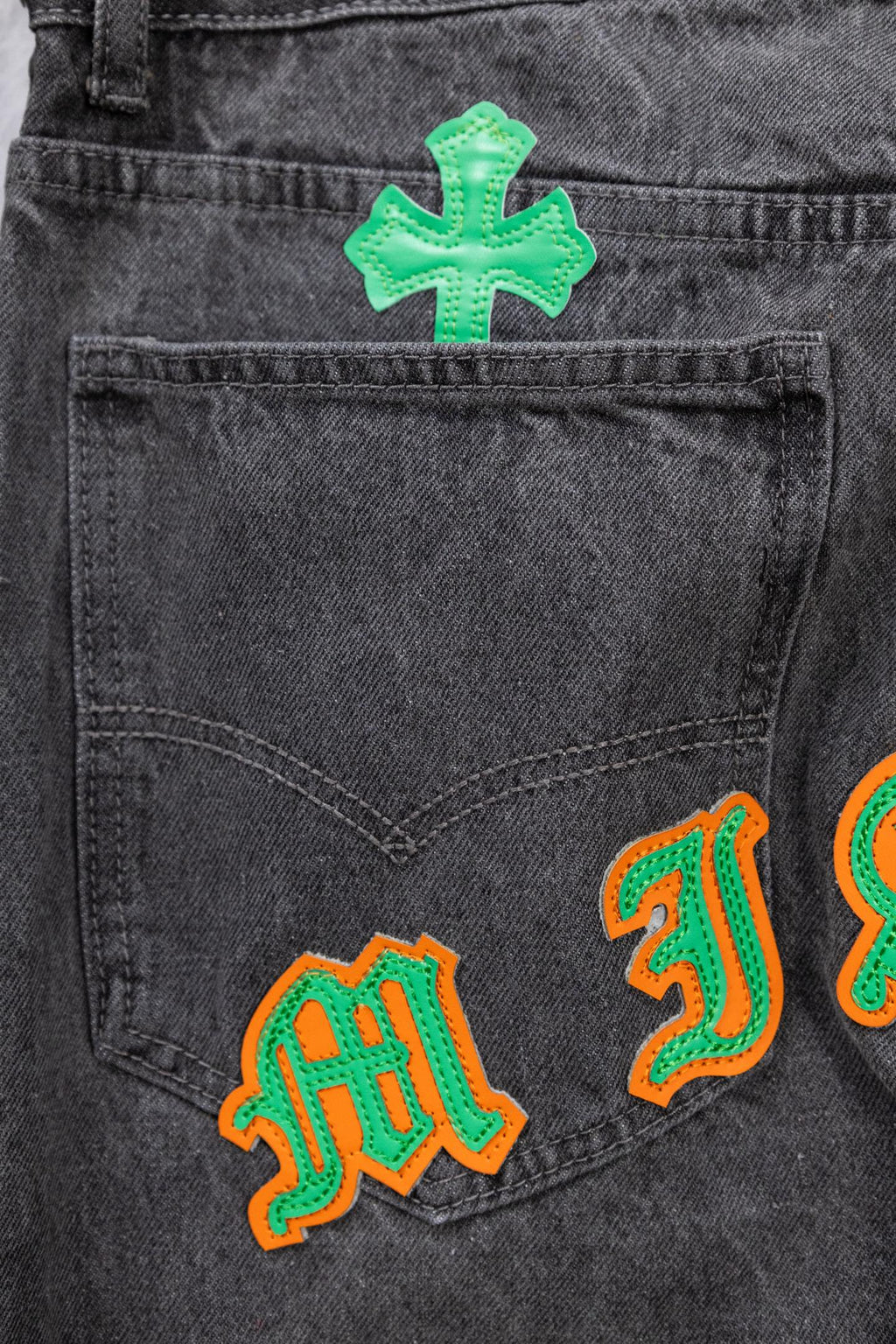 Dark gray denim pants with green cross and colorful embroidered patches