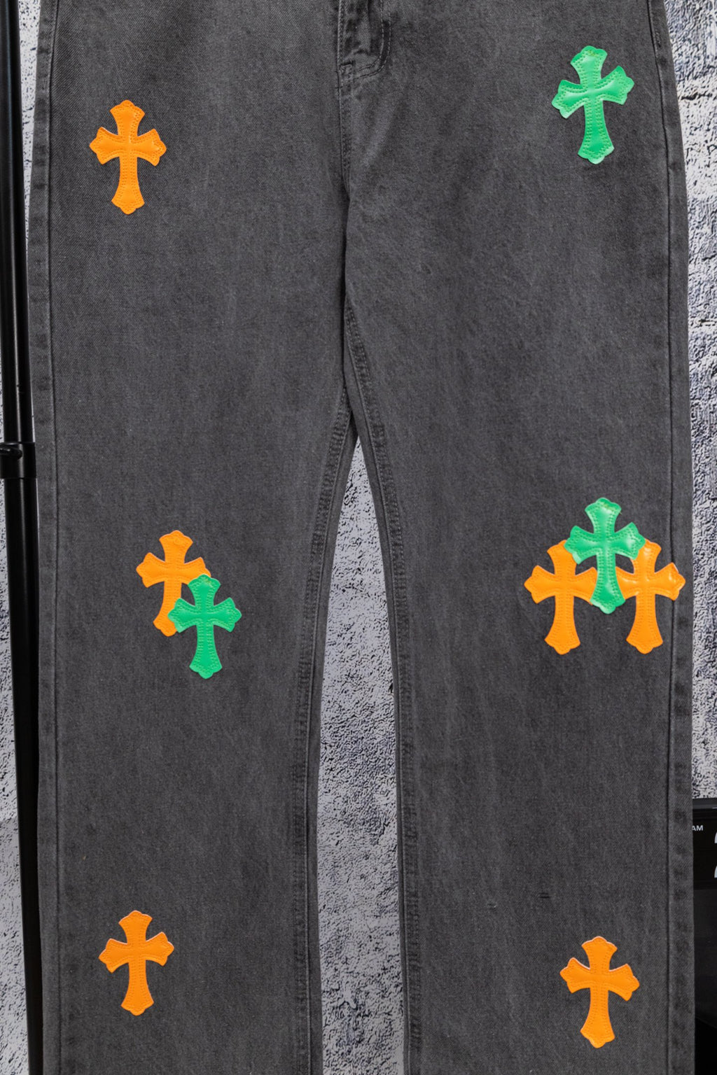 Dark gray denim pants with multiple green and orange cross patches on the legs