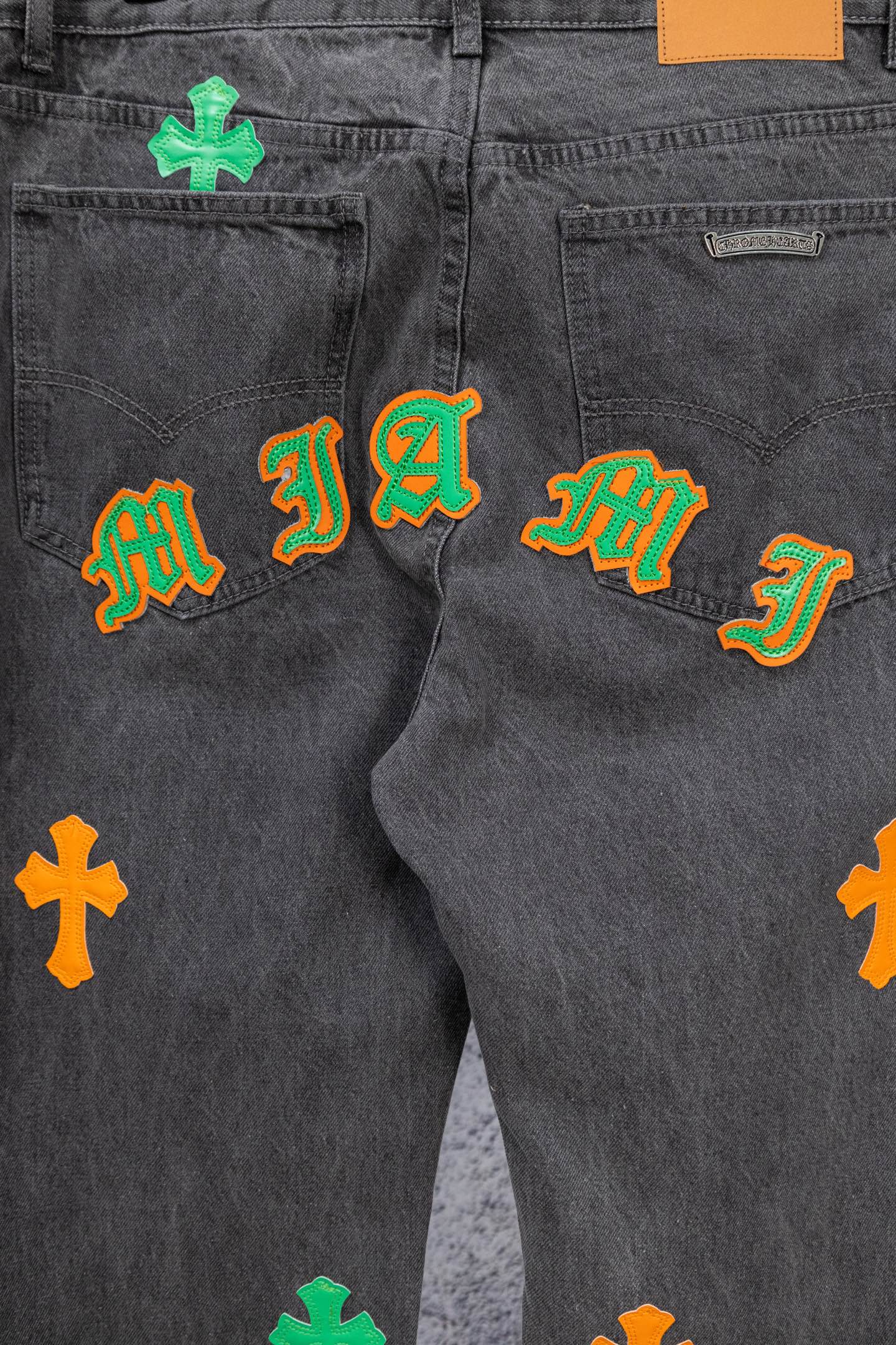 Dark gray denim pants with multiple embroidered symbols across pockets