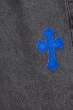 Chrome pants side close-up with a single blue cross applique on dark denim