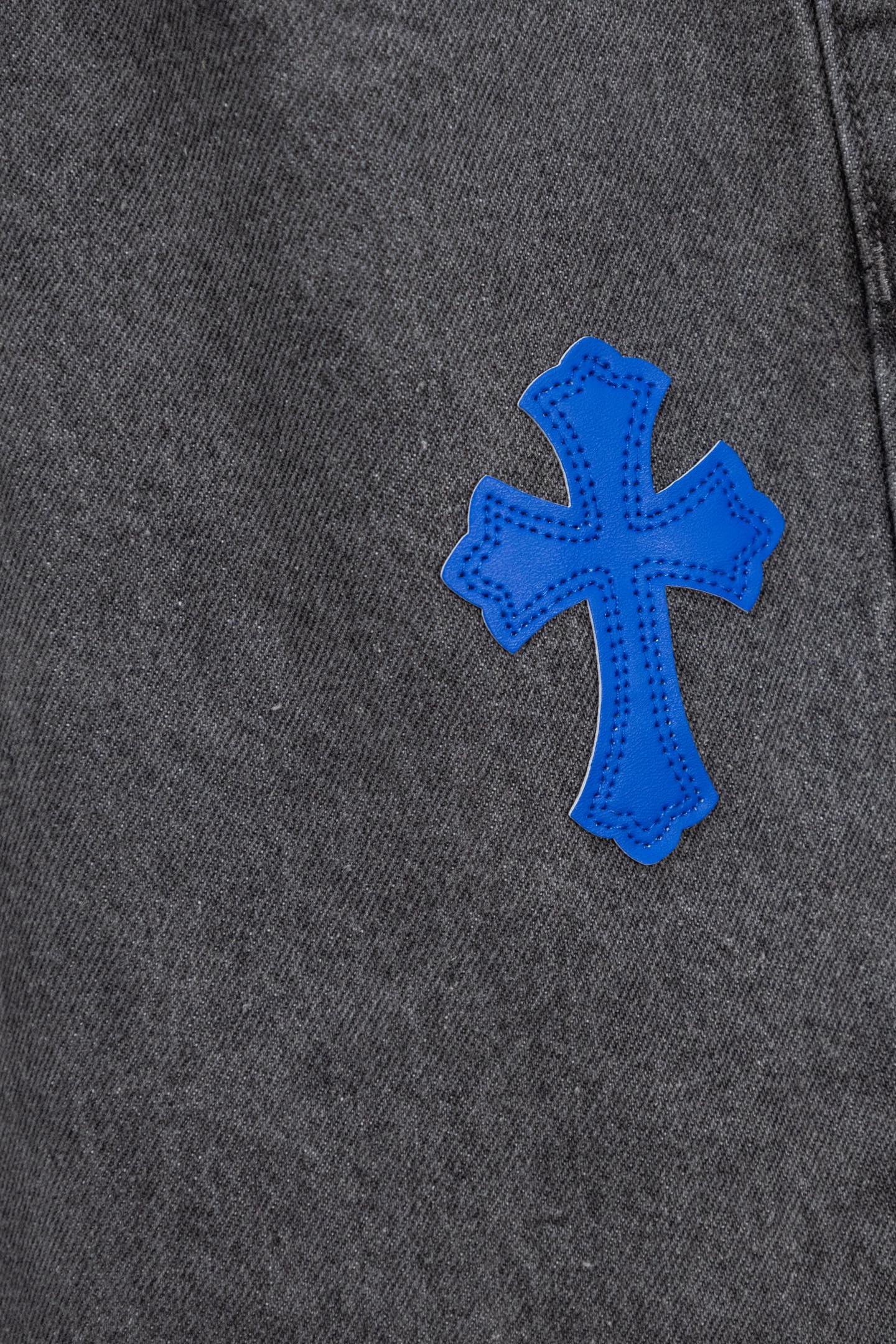 Chrome pants side close-up with a single blue cross applique on dark denim