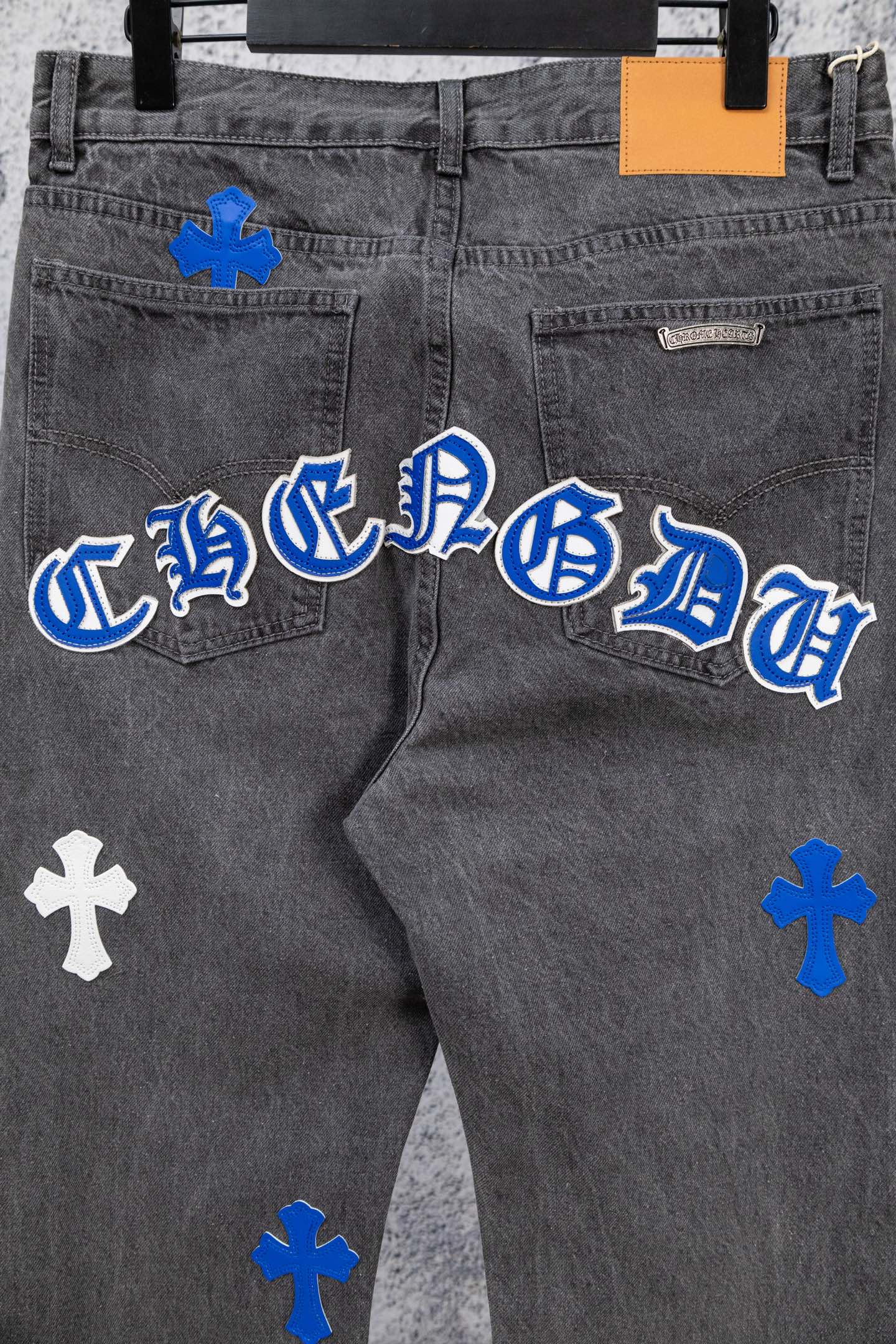 Close-up gray denim pants with blue-and-white cross graphic on the leg.