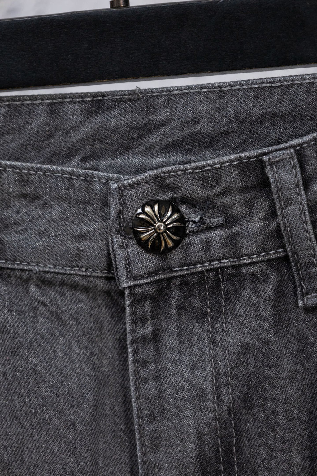 Gray denim pants close-up of decorative snap-button on waistband pocket.