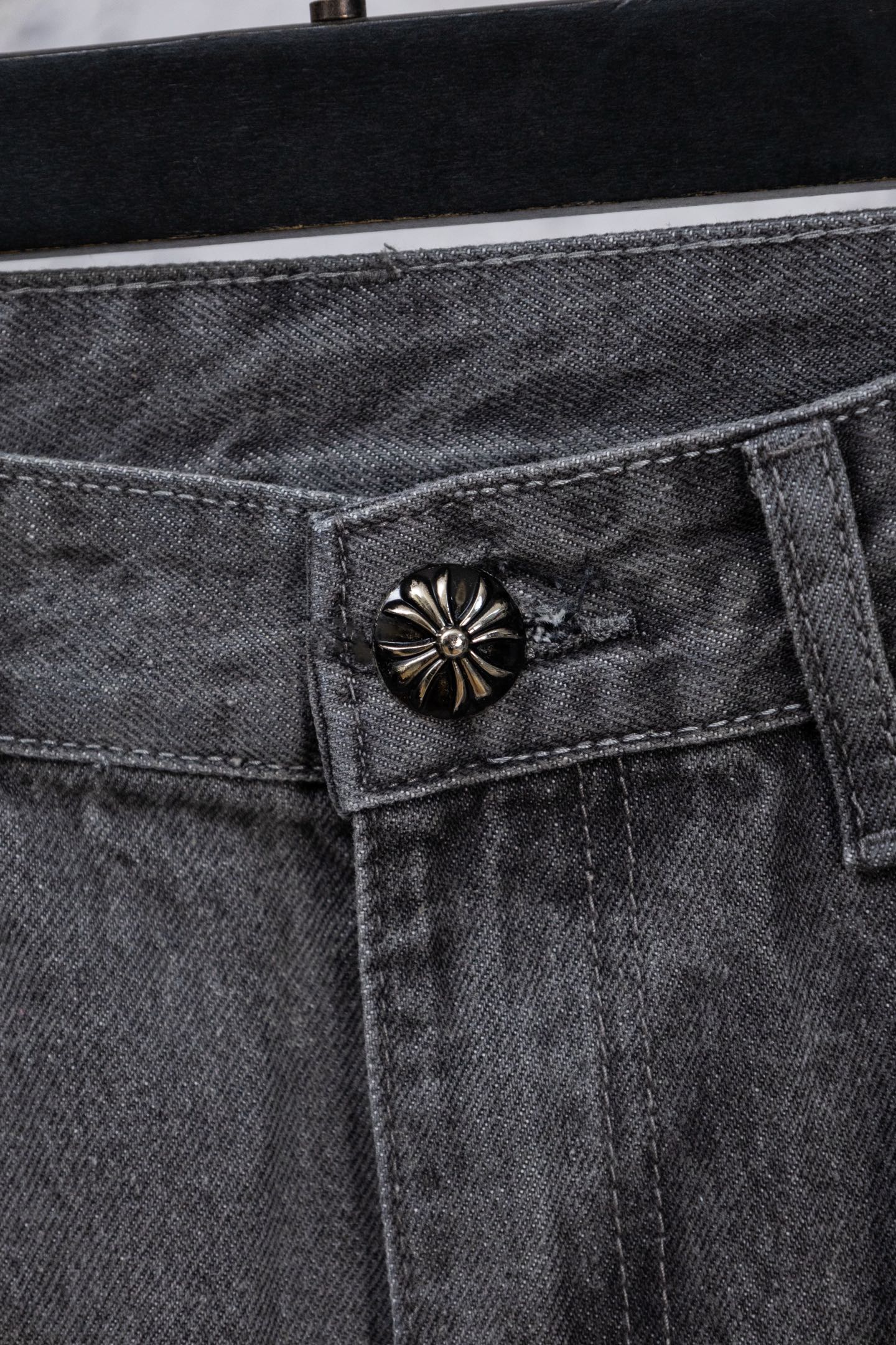 Gray denim pants close-up of decorative snap-button on waistband pocket.