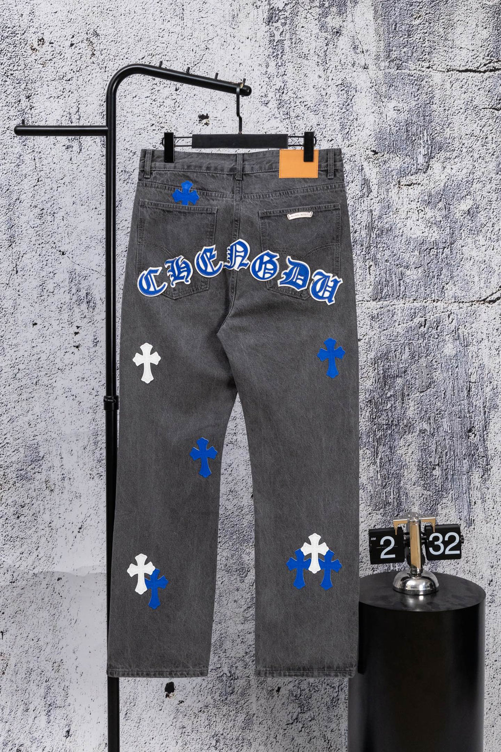 Gray denim pants with blue and white cross patches and orange size tag, front view.
