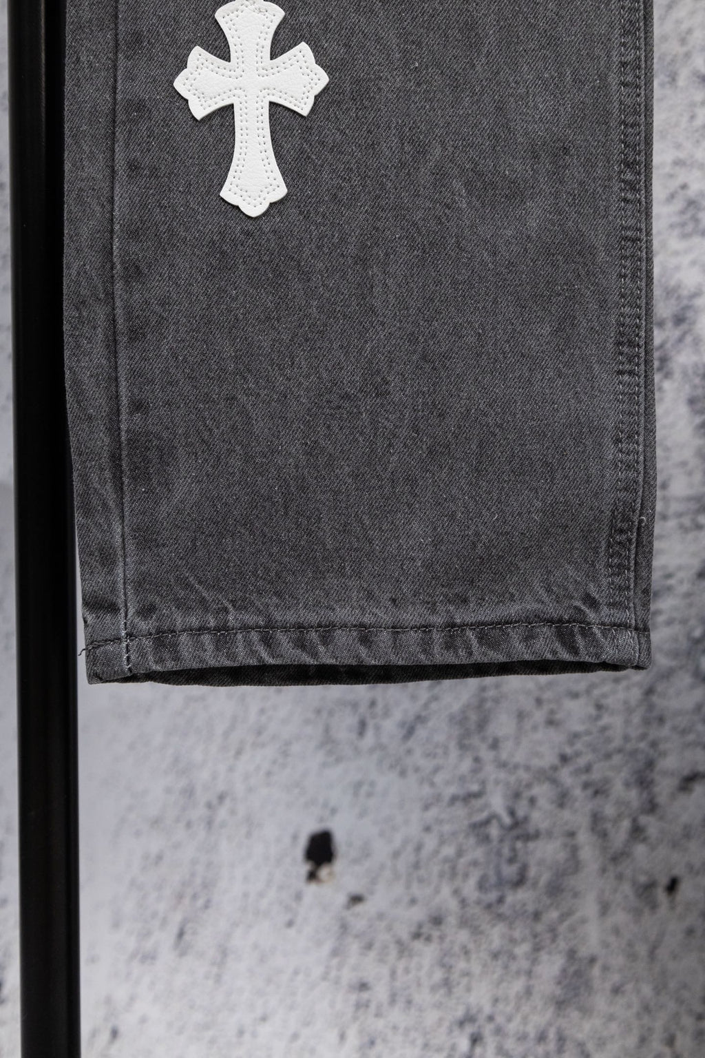 Gray denim pants close-up of a white cross patch on the hem.