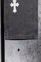 Gray denim pants close-up of a white cross patch on the hem.