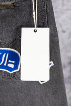 Chrome pants detail with hanging white tag and blue logo patch on dark denim
