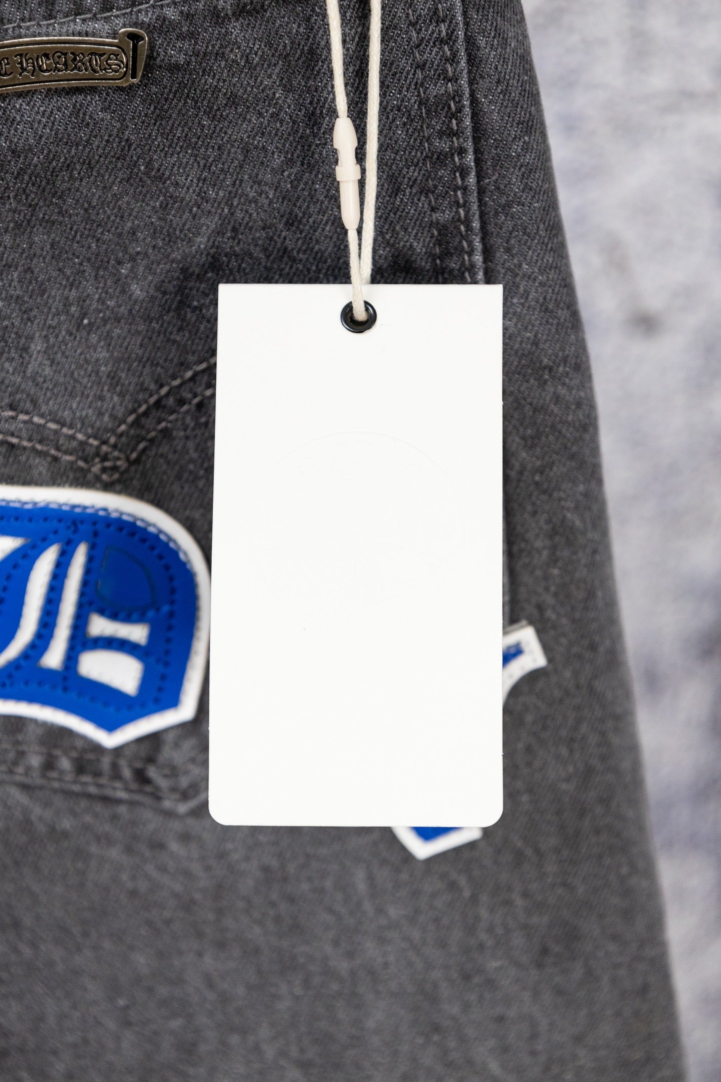 Chrome pants detail with hanging white tag and blue logo patch on dark denim