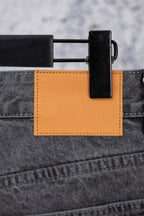 Chrome pants waistband detail with orange leather-like tag and dark clasp