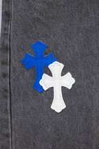 Gray denim pants close-up of a large blue-and-white cross applique on the leg.